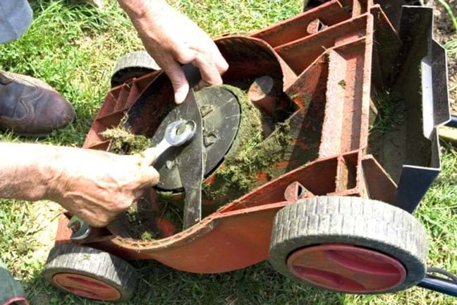 Man inspecting upside down mowers blades using a spanner