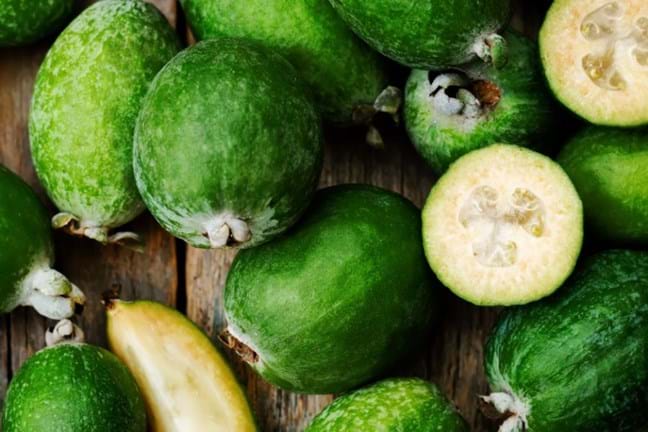 Feijoa fruit halved and whole on a wooden chopping board