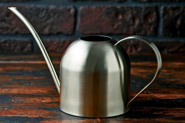 silver watering can with a long thin spout on a timber table